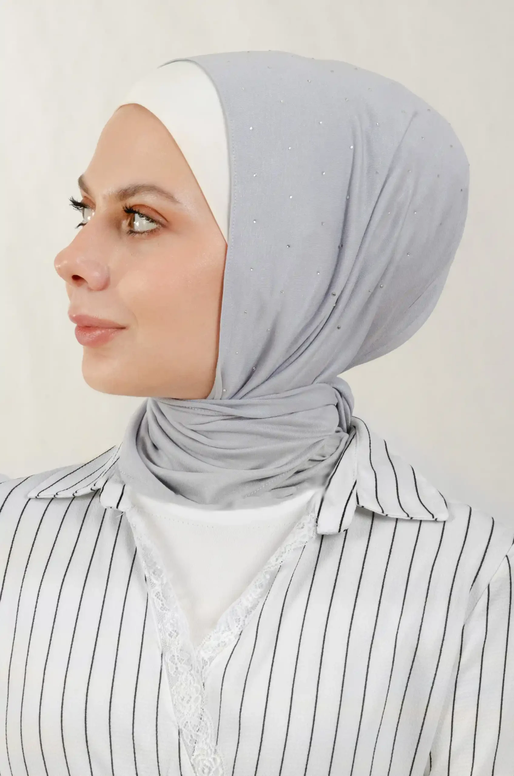 The DMC Strass Dots Grey Tiangle Shawl is a cozy, breathable triangle hijab made from cotton fabric with shimmering Strass details in grey. Perfect for both daily wear and special occasions.