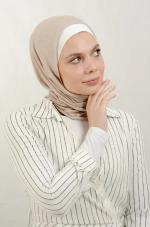 The DMC Strass Larva Beige Triangle Shawl is a cozy, breathable triangle hijab made from cotton fabric with shimmering Strass details in beige. Perfect for both daily wear and special occasions.