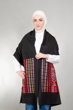 عارضة ترتدي شال كتف الشمال أحمر ميكس أسود بتطريز فلاحي بالأحمر والبرتقالي والأخضر الليموني والليلكي